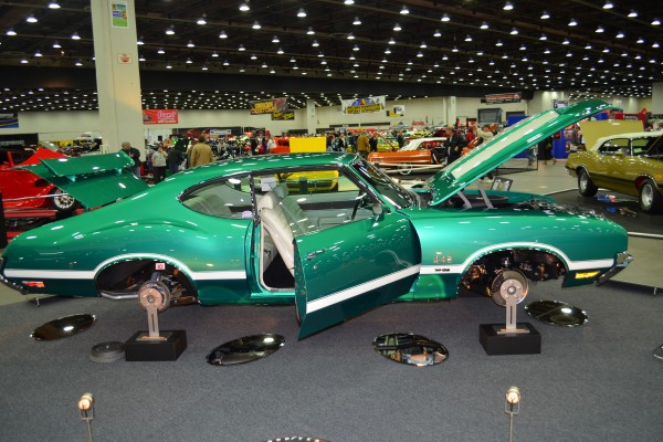 green cutlass 442 on display at an indoor car show with wheels off