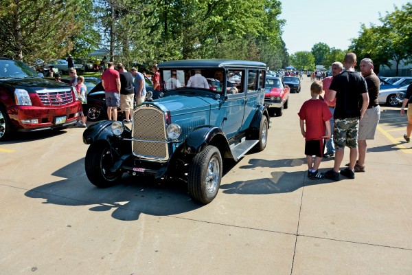 An old ford model A hot rod driving through a car show event