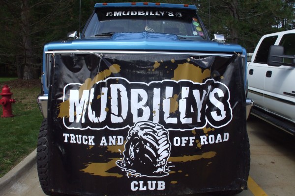lifted chevy truck at a car show with club banner