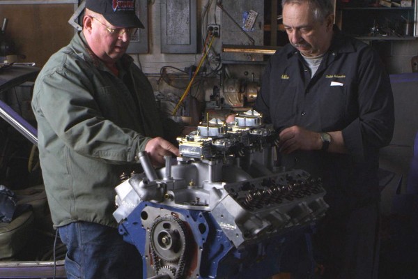 two men working on a ford v8 engine in a shop