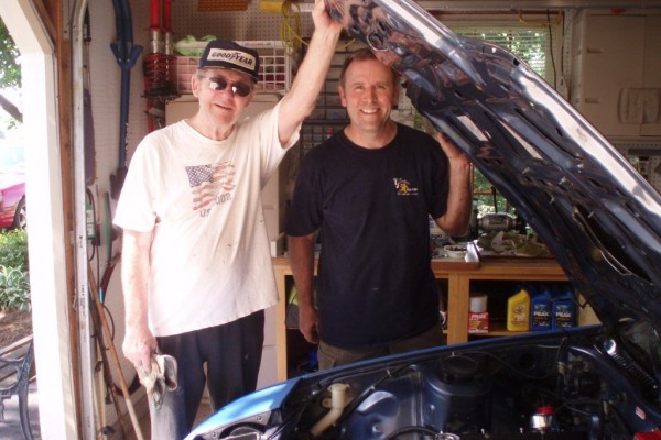 two men posing next to a sports car in a shop