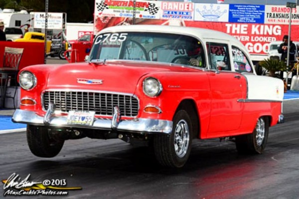 1955 chevy drag car doing a wheelstand at the strip