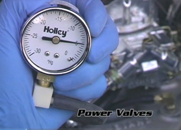 man holding a holley vacuum gauge near a carburetor