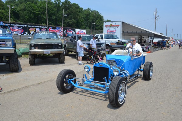 blue ford t bucket roadster being driven at a car show