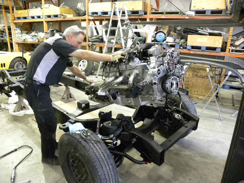 man lowering ls3 engine onto a hot rod frame