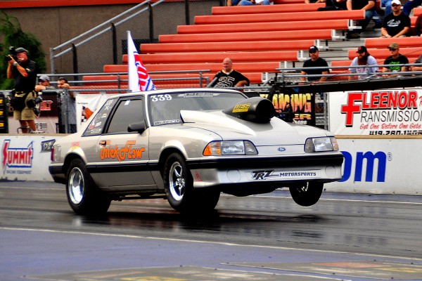 fox body ford mustang in trick flow livery launching at drag strip with wheel stand