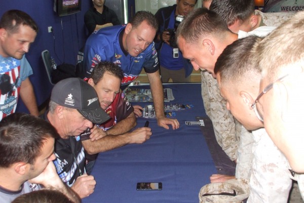 The team watches race footage on a cell phone with a member of the U.S. Marine Corps.