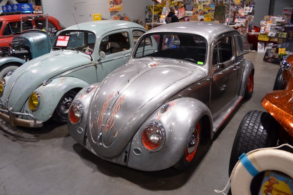 a pair of vintage customized Volkswagen beetles displayed at indoor car show