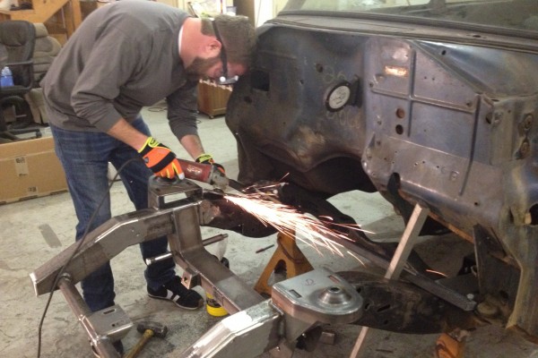 man grinding welds on a hot rod vehicle frame