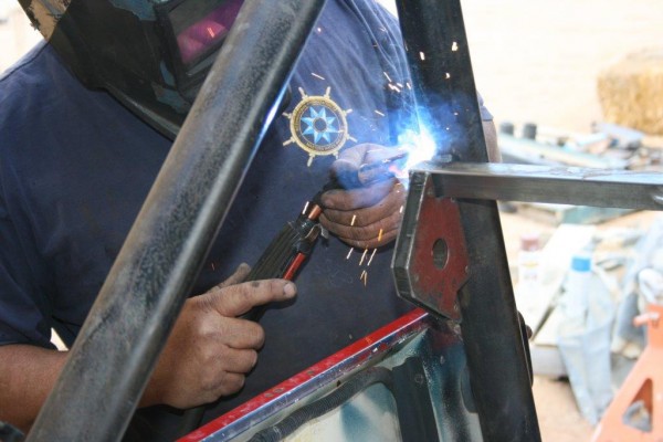 man welding a harness bar mount on a jeep cj roll bar
