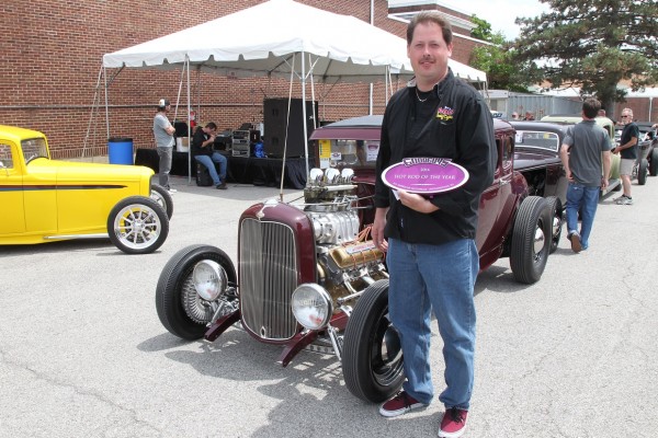 man holding goodguys hotrod of the year award near a ford coupe