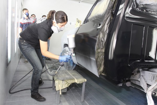 woman spraying black automotive paint onto a vintage truck door in a paint booth