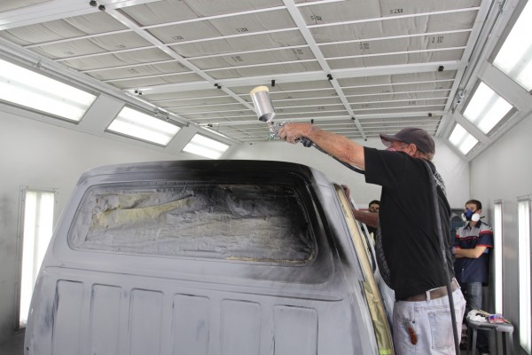 man painting a truck cab roof in a vehicle spray booth