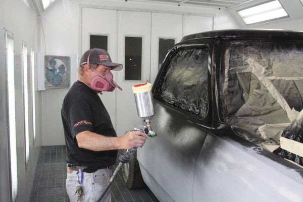 man painting a truck door in a vehicle spray booth