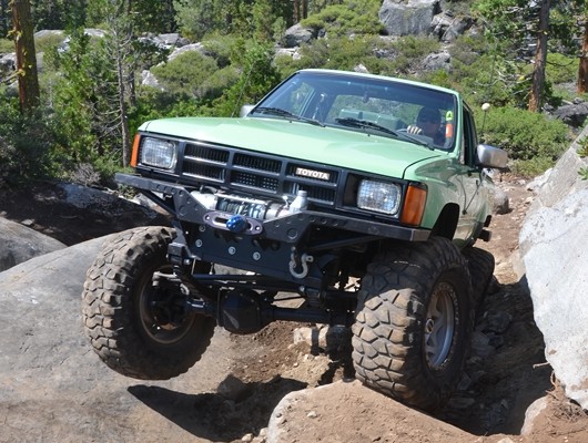 an off road modified toyota tacoma crawling up rocks on a trail