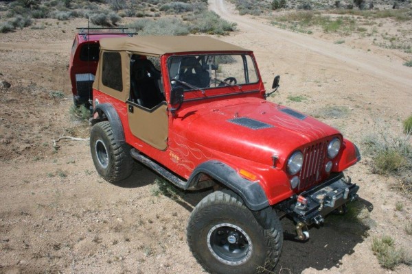 Red Jeep CJ 7 pulling a trailer on a desert trail