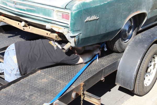 man securing an old project car to a trailer with a tie down strap