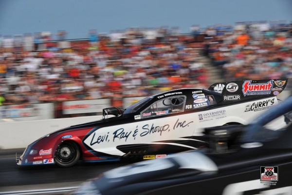 side by side view of two nhra funny cars racing down dragstrip