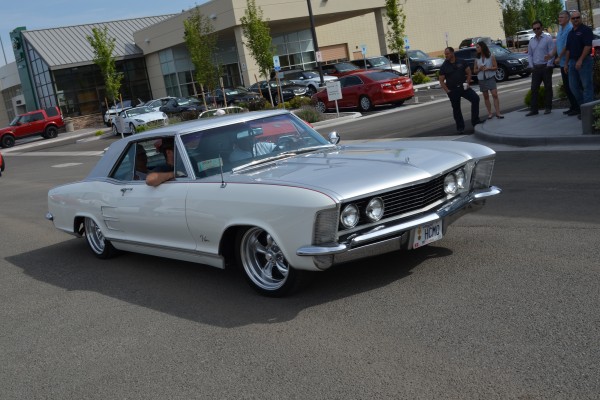 silver custom buick riviera entering parking lot of a car show