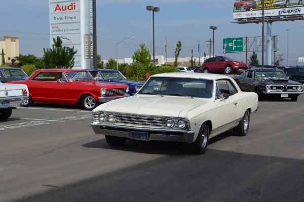 white first gen chevelle entering parking lot of a car show