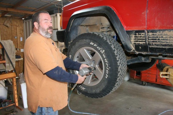 man removing wheel and lugnuts from a jeep cherokee xj on lift