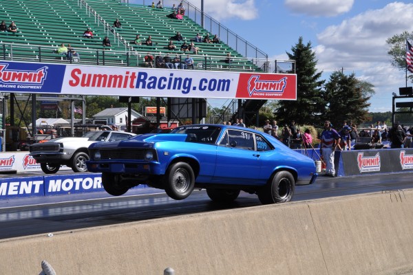 two vintage chevy musclecars doing wheelstands at a dragstrip