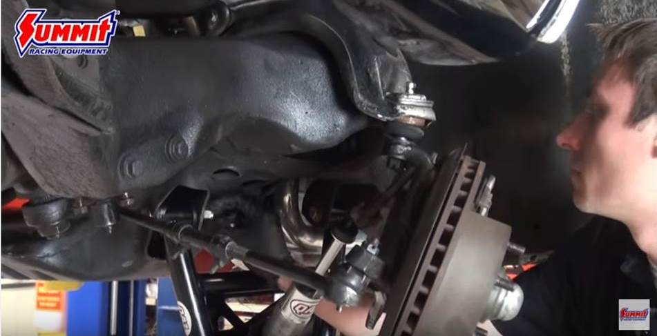 man installing shock on an old car