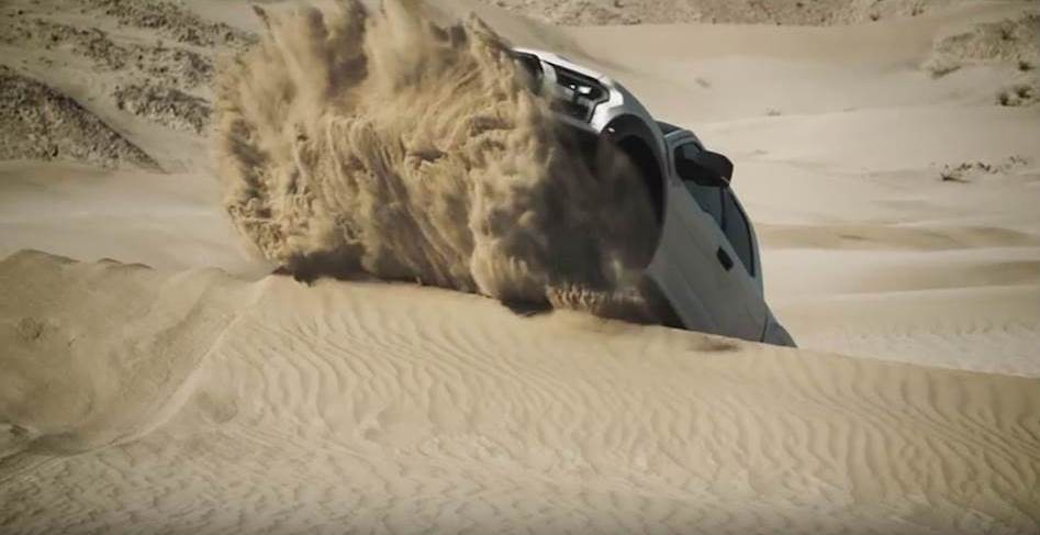 ford raptor climbing up a sand dune