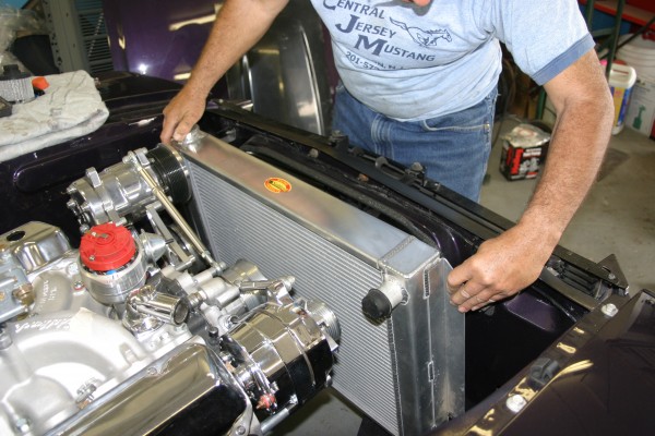 man installing a radiator in a vintage mustang