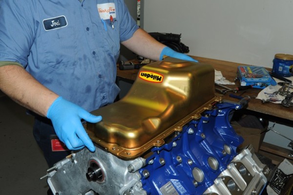 man fitting milodon oil pan on ford modular v8 engine