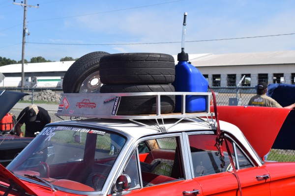 old car with roof rack containing race tires and utility jug