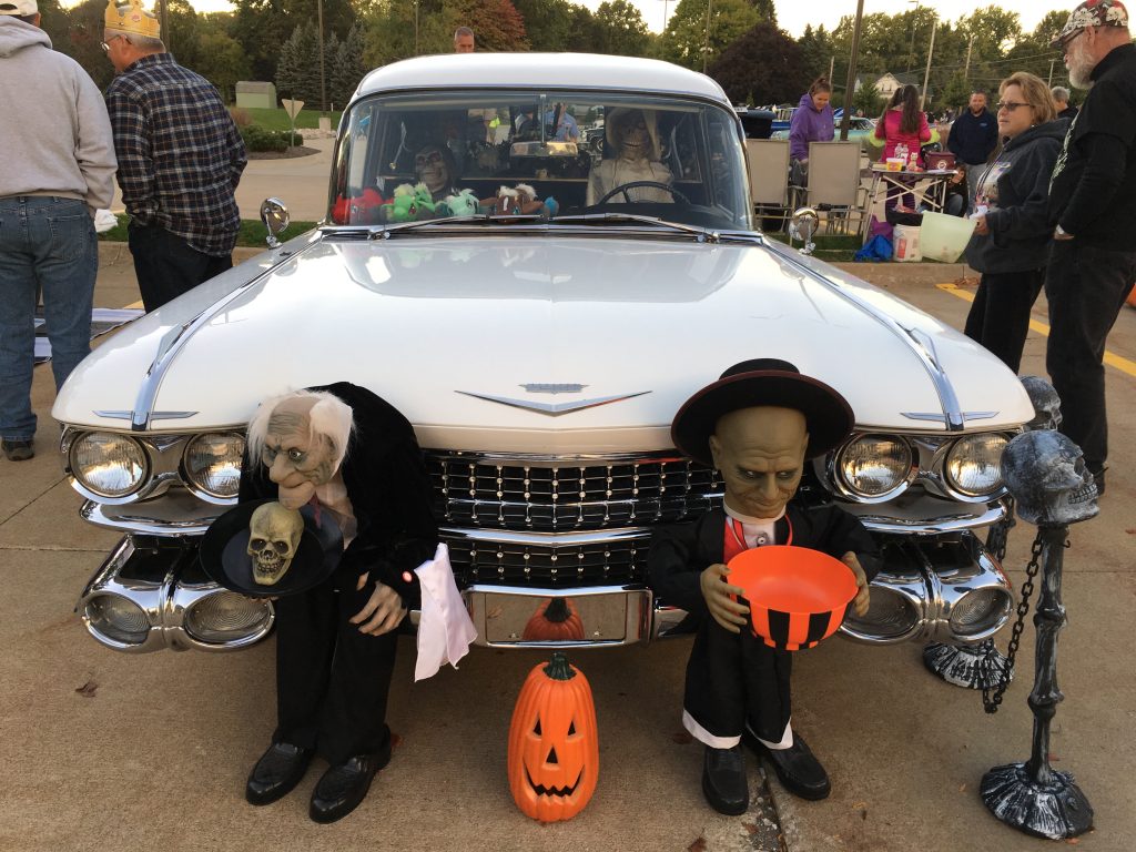 creepy Halloween decorations near a vintage hearse at a car show