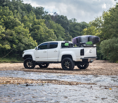 white chevy truck parked near stream with kayak rack