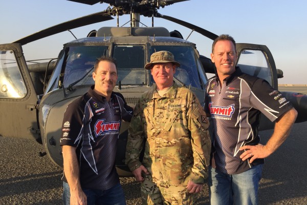 greg anderson and jason line pose with troops near helicopter