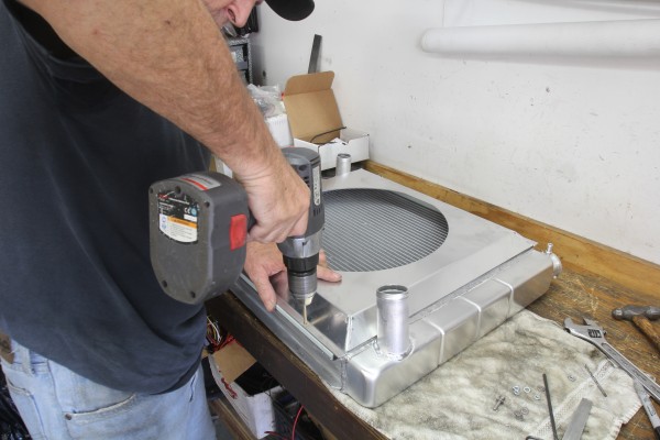 man drilling holes to install a fan shroud on radiator