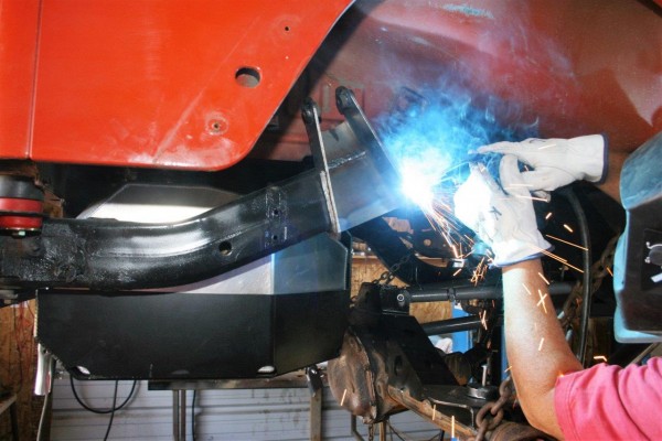 man welding a bracket on a jeep frame