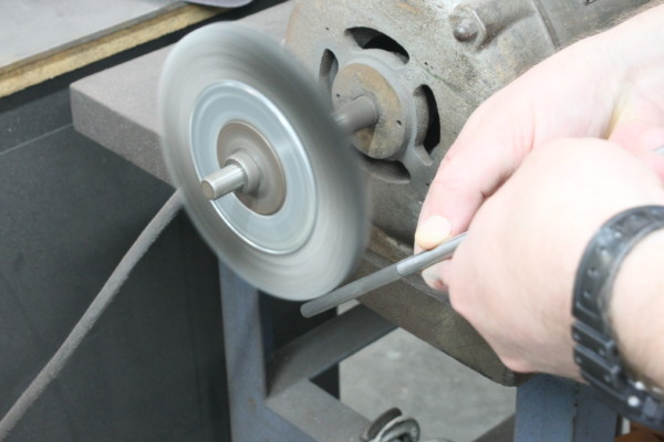 deburring a metal shaft on a brush grinder wheel