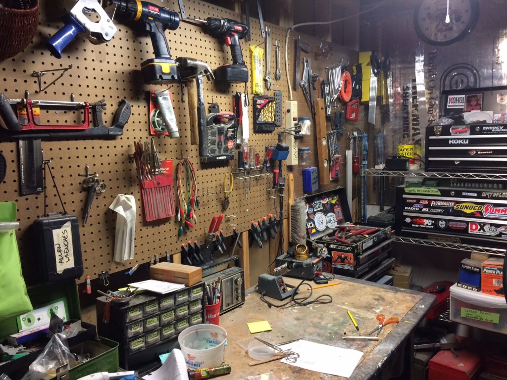 crowded workbench with hand and power tools on pegboard next to tool box