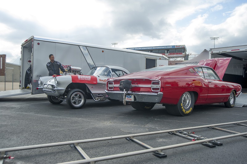 a pair of vintage corvette and torino drag cars near race trailers