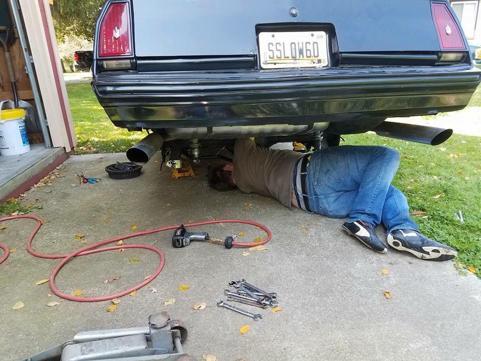 man working underneath a vintage chevy monte carlo muscle car