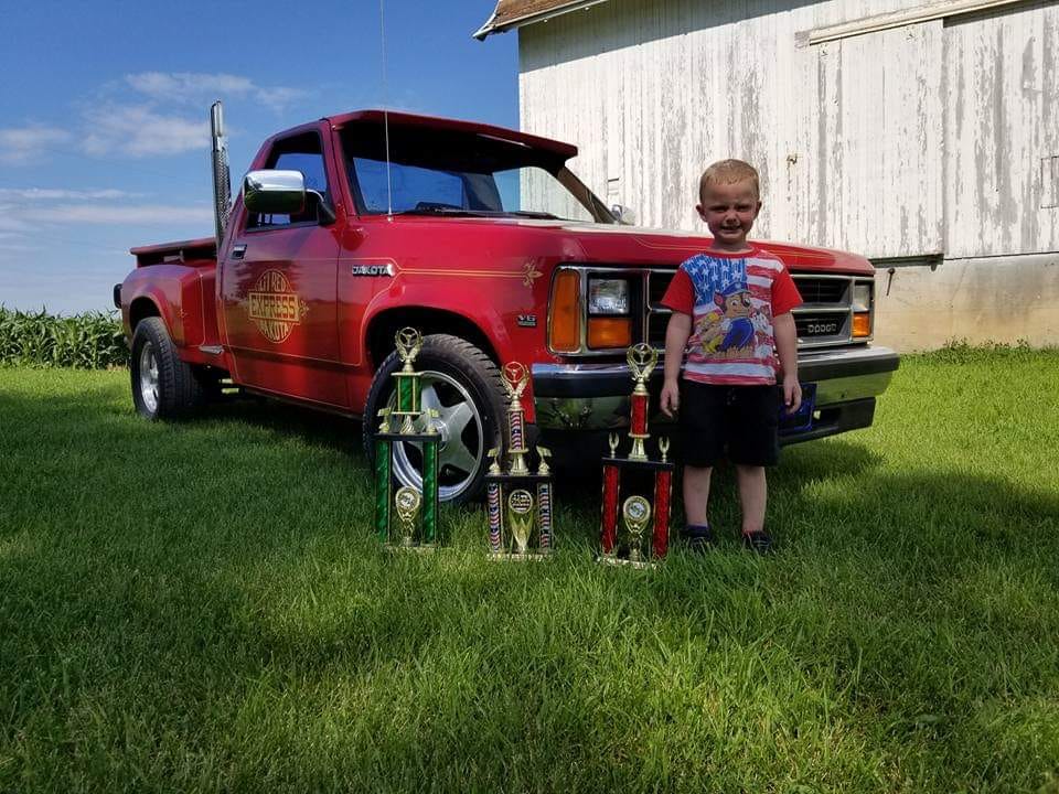 young boy standing next to trophies and dodge lil red express truck