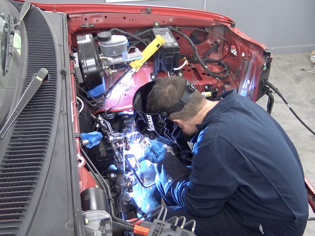 man welding parts inside a truck's engine bay