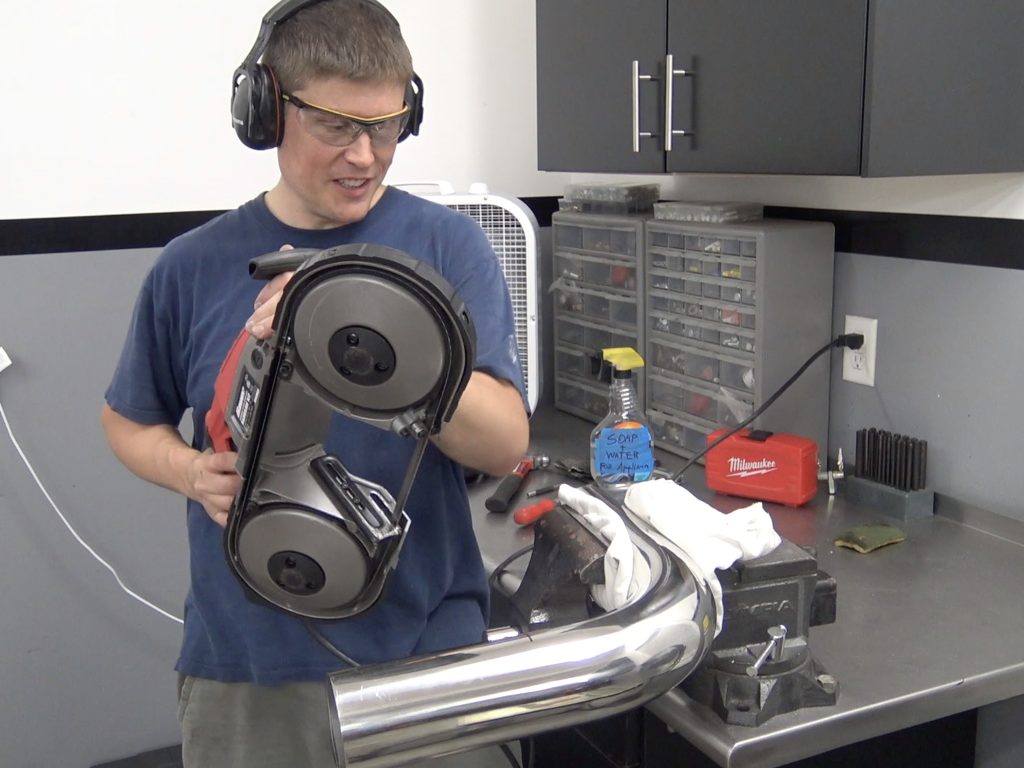 man using a handheld band saw to cut stainless steel exhaust tubing