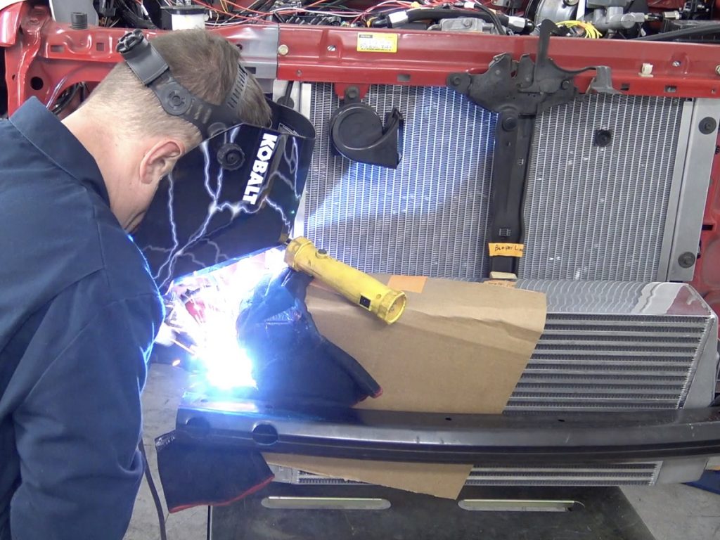 man welding intercooler brackets onto a toyota tacoma truck with an ls engine swap