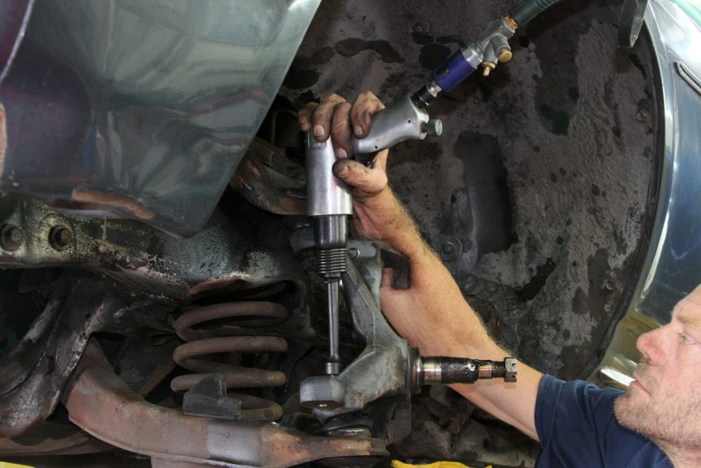 a man removing a steering knuckle from a car using an air tool