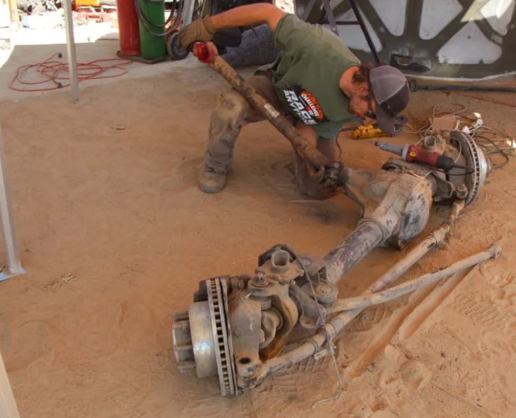 man in a junkyard removing driveshaft from a rear axle assembly
