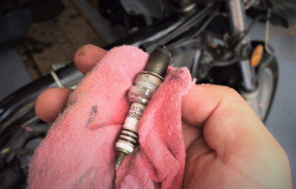 man holding a used dirty spark plug in a shop rag