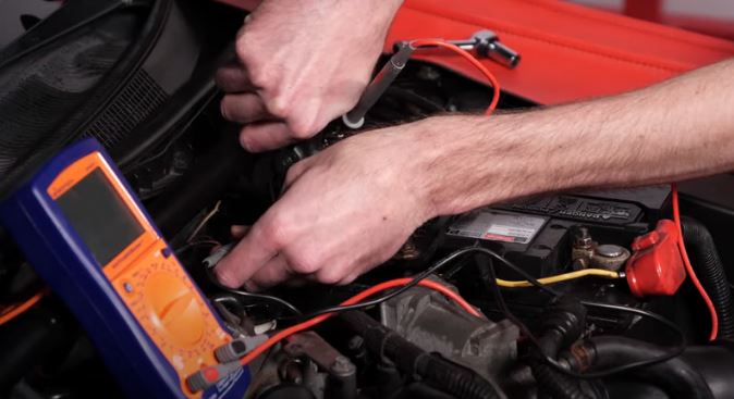 man checking amp current draw on a car battery with a multimeter