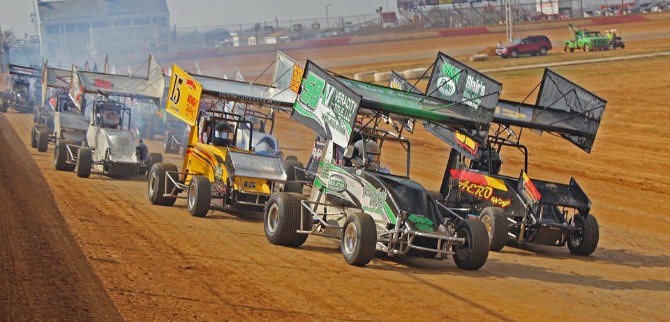 a cluster of sprint race cars on a dirt circle track course