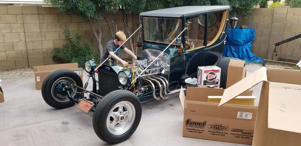 younf man making adjustments to an engine in a t bucket hot rod